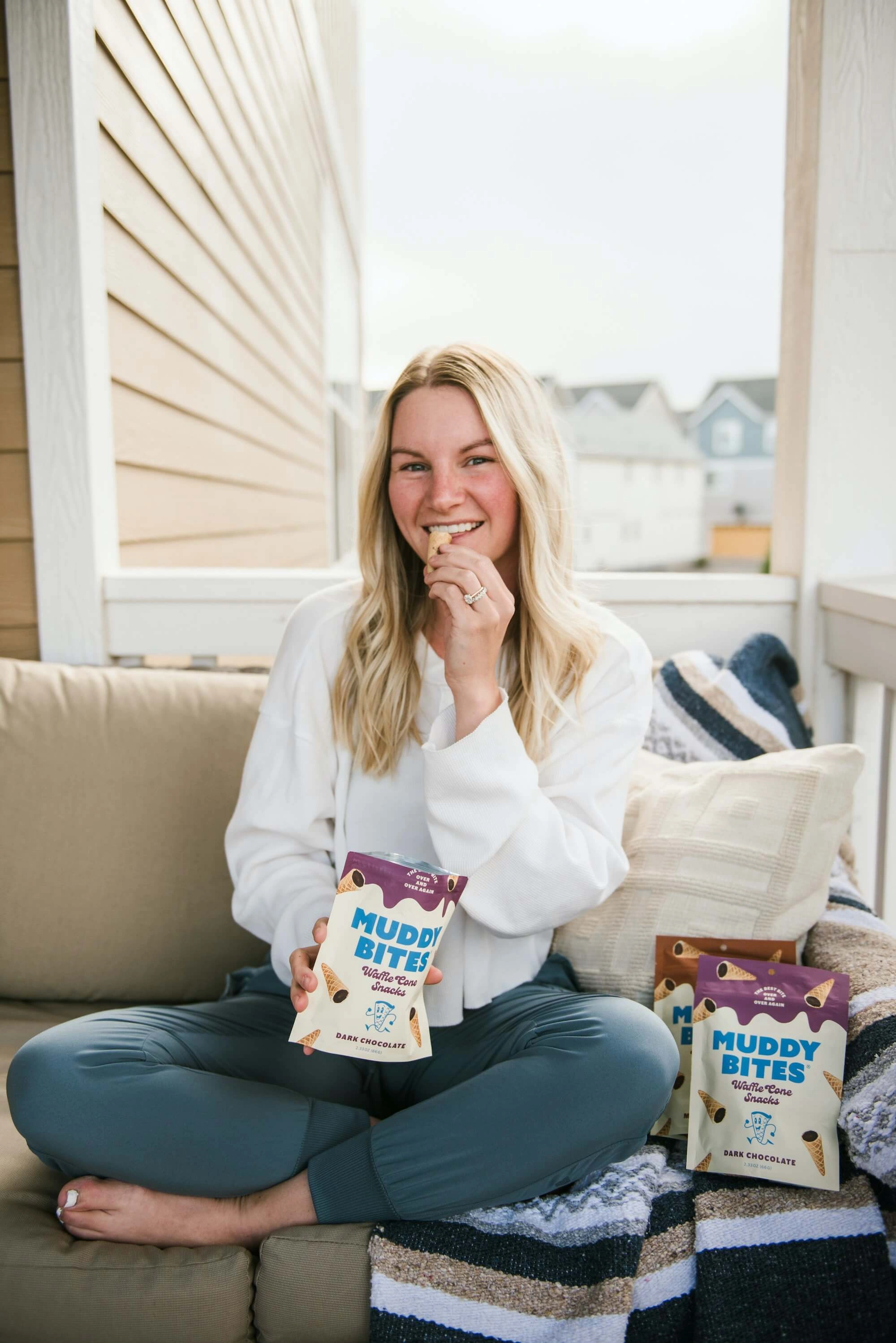 A woman sitting on a couch with bags of Muddy Bites