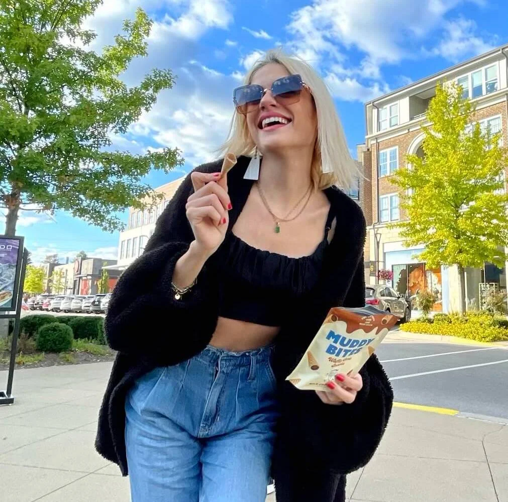 A woman outdoors holding a bag of Muddy Bites